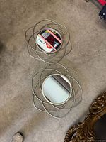 Two geometric metal framed round mirrors on carpeted floor showing floral loop design and reflective surfaces