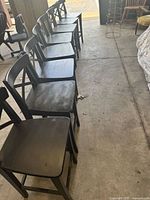 Six black wood cross back bar stools arranged in a row showing seating surfaces and legs.