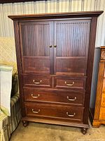 Closed front view of the wooden armoire with two doors and four drawers, showing dark brown finish and brass hardware.