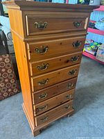 Front view showing tall chest with 7 drawers, brass handles and natural/stained pine finish.