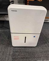 Front view of white Toshiba dehumidifier showing front panel with brand name and water level indicator slot.