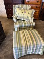 Full view of armchair with ottoman and floral accent pillow, showing striped upholstery and skirted base.