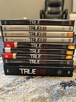 Stack of True Blood DVD cases showing disc numbers and episode ranges for Seasons 1, 2, and 3, total of 13 discs.