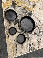 Four cast iron skillets arranged on carpet showing various sizes in the set.