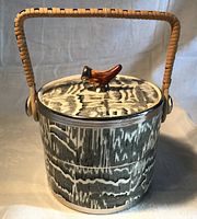 Front view of ceramic biscuit barrel showing glaze pattern, bird finial, handle and metal mounts