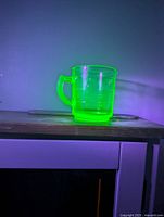 Cup glowing bright green under UV, showing uranium content