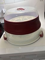 Front view of round plastic carrier showing clear lid, red collar, side latch