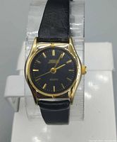 Front view showing gold-tone case, black dial, gold markers, black strap