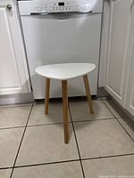 Full view of small white triangular side table with wood legs