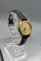 Front angled view showing gold-tone case, cream dial, Arabic numerals, black strap