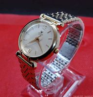 Left profile view on stand showing gold-tone case, white dial and link bracelet