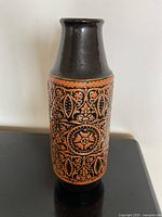 Full view of vase showing cylindrical form, orange and black relief design, glossy black neck