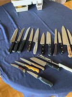 Full view of fourteen kitchen knives laid out on blue cloth showing sizes and styles