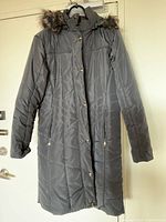 Front view of long black quilted hooded coat showing buttons, zipper, pockets