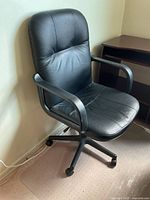 Front angled view of black pleather swivel office chair with armrests and wheeled base