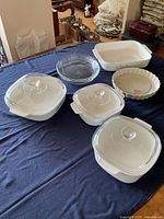 All items laid out on table: three lidded square casseroles, clear pie plate, fluted ceramic dish, rectangular baker