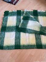 Full view of green, beige and white plaid throw blanket laid flat