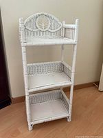 Front view of white wicker stand showing three shelves and decorative arch