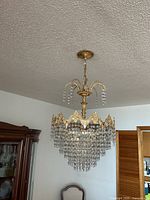 Full view of chandelier hanging unlit showing gold frame and crystal tiers