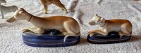 two unmarked reclining greyhound figurines on blue bases