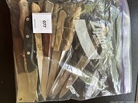 Steak knives in a zip-style plastic bag with wood-style handles and serrated blades.