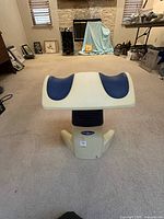 Front view of the Back2Life lower-back therapeutic motion device showing its white base, black flexible middle section, and the contoured white top with two blue cushioned areas.