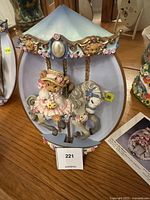 Front view of the wall-mounted carousel bear figurine showing the pastel blue canopy, floral detail, teddy bear in bonnet and dress riding carousel horse.
