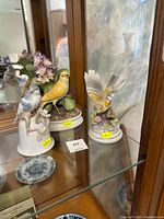 Three porcelain bird figurines displayed in a cabinet, showing overall group and arrangement