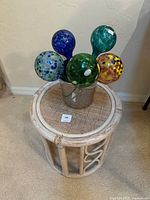 Top-down view showing all five colorful watering globes arranged in metal bucket on rattan table.