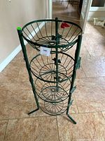 Full view of green metal wire stand with four circular baskets, showing overall stand and design including legs and leaf decorations.