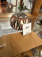 Front and side view of a rounded pottery seed pot with black and rust geometric designs on white, placed on a shelf with price tag $48.