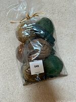 Photo of sealed bag containing a variety of decorative spheres in earthy green and brown tones with mixed textures including woven and solid felt spheres.