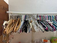 Shows natural wood hangers, velvet hangers, clear plastic hangers with clips, and multi-colored plastic tube hangers hanging on a rack.