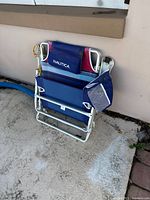 Side view of Nautica branded folding beach chair showing aluminum frame, fabric seat and backrest with logo, mesh side pocket and carrying strap.