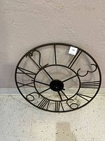 Full view of outdoor round metal wall clock with open frame and Roman markers