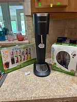 Black SodaStream soda maker, flavor sampler box, and bottle set displayed on countertop.