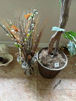 Tall faux ficus tree and natural-look decorative bundle side by side on floor.