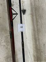 Photo of the lower portions of two fishing rods leaning against a concrete wall, showing rod handles and guides, one with visible wear and old label remnants.