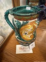 Side view of the colorful glazed ceramic pitcher showing ornate painted design and sculptural handles.