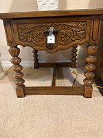 Close-up of side table front showing carved drawer front with leaf motif, barley twist legs and pegged joinery at base.