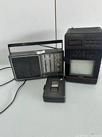 Photo showing the full view of all three vintage electronic items together: a stereo cassette player, a multi-band radio, and a clock radio/TV combo unit.