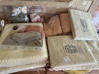 Photo showing unopened lace curtain panels, cream crochet bedspread in packaging, peach linens, and Ziploc bags with additional vintage linens and fabrics