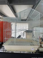 Side front view of the vintage white metal birdcage with pagoda roof showing the removable plastic base tray and decorative scrollwork on the cage bars.