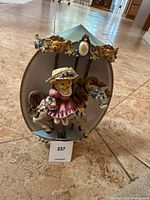 Front view showing teddy bear in Victorian dress on carousel horse with pastel blue canopy and golden floral details.