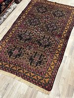 Full view of the Baluchi rug laid on wooden floor, showing overall pattern and design.