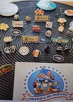 Overview of assorted pins on woven mat including Disney America on Parade sticker and multiple pins