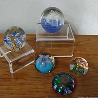 Group shot of all five glass paperweights on wooden surface with acrylic stands