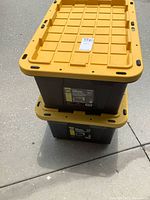 Two stacked black totes with yellow lids