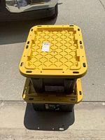 Two stacked black totes with yellow lids on driveway