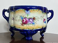 Front view showing cobalt blue jardiniere with floral panel and footed base